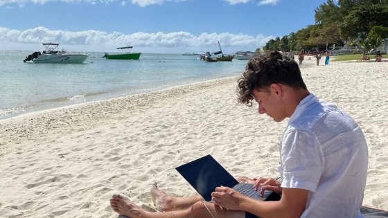 Student sitting on the beach with his laptop